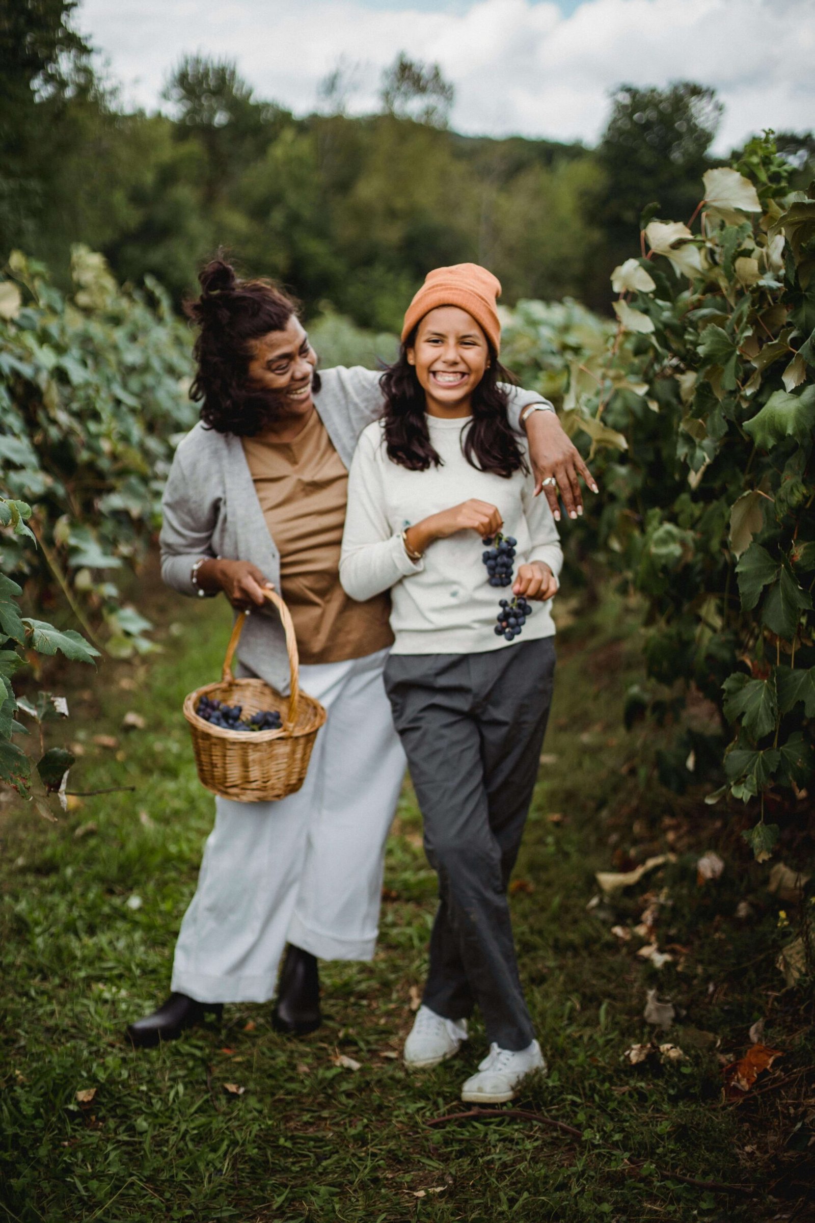 Cheerful ethnic gardener with daughter on path in vineyard. jenniferanistonbody.com